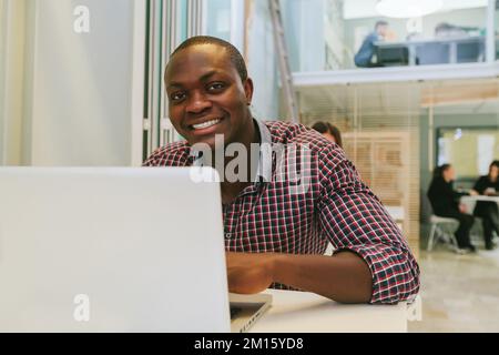 Schwarzer Mann, der mit einem Laptop auf einem Holztisch arbeitet Stockfoto