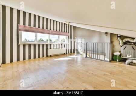 Ein leeres Wohnzimmer mit Holzfußboden und gestreiften Tapeten an den Wänden in Schwarz-Weiß-Streifen Stockfoto