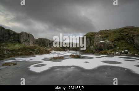 Foggintor Quarry, Dartmoor National Park, Devon, Großbritannien. 10.. Dezember 2022. UK Weather: Der See des Foggintor Steinbruchs war fest gefroren, und auf dem Eis bildete sich ein Staub von frischem Schnee, der sich kreisförmig umgab. Die bitterkalten Bedingungen werden sich an diesem Wochenende fortsetzen, mit mehr Schneevorhersage über das Moor. Kredit: Celia McMahon/Alamy Live News Stockfoto