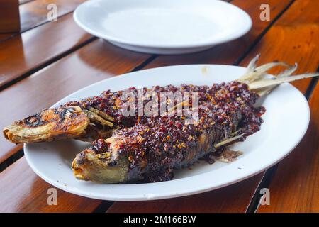 Gebratener Milchfisch mit scharfer Chilisauce und Garnelenpaste auf einem weißen Teller Stockfoto