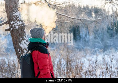 Ein Mann im Winter atmet draußen eine Wolke aus Dampf und Rauch aus Stockfoto