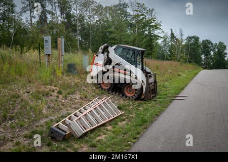 Mini-Frontlader mit Gabelstapleranbau neben einer gepflasterten Straße mit zwei Leitern auf einer neuen Baustelle. Stockfoto