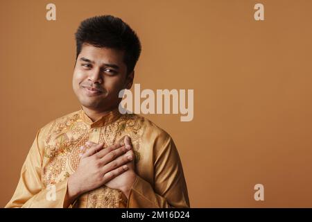 Ein junger indianer, der lächelt und Händchen an seinem Herzen hält, isoliert auf gelbem Hintergrund Stockfoto