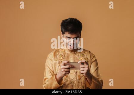 Junger brauner indianer, der lächelt und ein Handy benutzt, isoliert auf gelbem Hintergrund Stockfoto