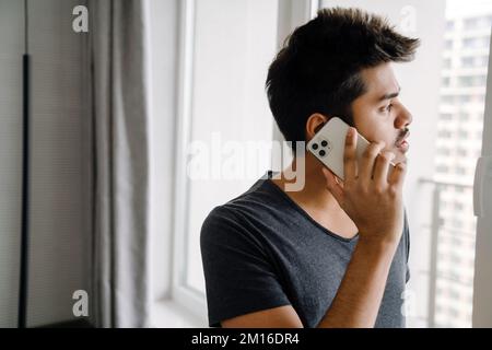 Ein hübscher, junger indianer, der zu Hause aus dem Fenster guckt Stockfoto