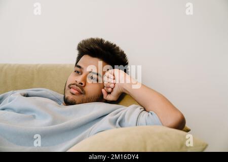 Ein langweiliger junger indischer Mann, der zu Hause auf dem Sofa sitzt Stockfoto