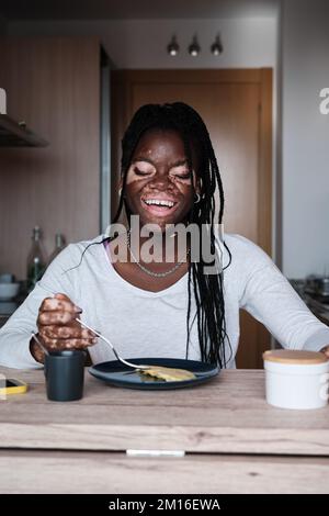 Fröhliche schwarze Frau frühstückt in der Küche Stockfoto