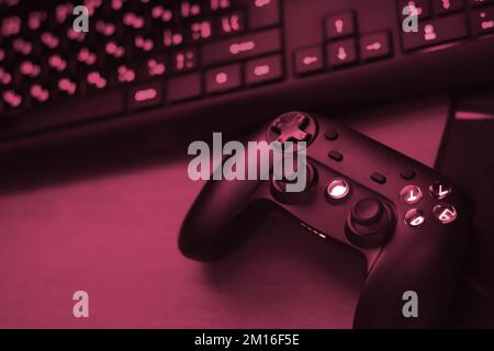 Modernes Gamepad mit pc-Tastatur auf dem Tisch in dunkler Nahaufnahme der Spielzimmerszene. Gameplay-Streaming und Rundgänge zu Videospielen Konzept Image Toned in Viva Magenta, Farbe des 2023. Jahres Stockfoto