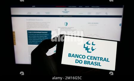 Person, die ein Mobiltelefon mit dem Logo der Zentralbank Banco Central do Brasil (BCB) auf dem Bildschirm vor der Webseite hält. Konzentrieren Sie sich auf das Display des Telefons. Stockfoto