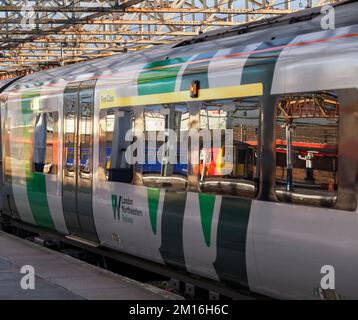 Der Zug der East Midlands Railway-Klasse 156 spiegelt sich im Fenster eines West Midlands Railway-Zuges der Klasse 350 am Bahnhof Crewe, Großbritannien, wider Stockfoto