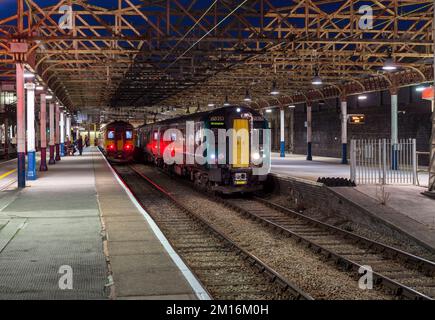 London North Western Railway und East Midlands Railway warten auf die Abfahrt vom Bahnhof Crewe bei Nacht. Stockfoto