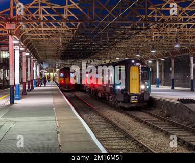 London North Western Railway und East Midlands Railway warten auf die Abfahrt vom Bahnhof Crewe bei Nacht. Stockfoto