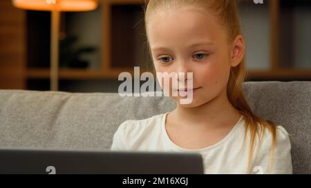 Liebenswert preteen kleines Mädchen sitzt auf der Couch mit modernen Laptop zu Cartoon-Film lustige Video Blick auf Computer-Bildschirm lachen studieren onli zu sehen Stockfoto