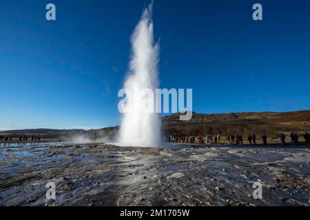 Allgemeiner Blick auf den Geysir Strokkur im geothermischen Park Haukadalur. Die geothermische Region in der Nähe des Flusses Hvitá und der Stadt Reykjavík beherbergt den geothermischen Park Haukadalur. Hier befindet sich Strokkur, einer der berühmtesten Geysire Islands, der im Durchschnitt alle 4 bis 8 Minuten ausbricht, mit einer durchschnittlichen Höhe von 15 bis 20 Metern, manchmal bis zu 40 Meter. Im Park gibt es mehrere geothermische Merkmale wie Schlammbecken, Fumarolen, Algenablagerungen und andere Geysire daneben und um ihn herum. Stockfoto