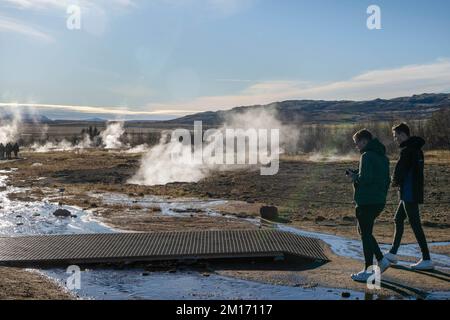 Reikiavik, Island. 21.. Okt. 2022. Man sieht Menschen, die in der Nähe der Fumarolen im geothermischen Park Haukadalur spazieren gehen. Die geothermische Region in der Nähe des Flusses HvitÃ und der Stadt ReykjavÃ-k beherbergt den geothermischen Park Haukadalur. Hier befindet sich Strokkur, einer der berühmtesten Geysire Islands, der im Durchschnitt alle 4 bis 8 Minuten ausbricht, mit einer durchschnittlichen Höhe von 15 bis 20 Metern, manchmal bis zu 40 Meter. Im Park gibt es mehrere geothermische Merkmale wie Schlammbecken, Fumarolen, Algenablagerungen und andere Geysire daneben und um ihn herum. (Bild: © Jorge Castellanos/SOPA Images V Stockfoto