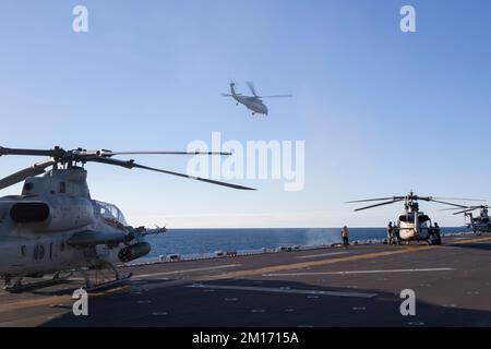 221208-N-VJ326-1050 PAZIFIK (8. Dez. 2022) – ein MH-60s Sea Hawk Hubschrauber, der dem Helicopter Sea Combat Squadron (HSC) 23 zugeteilt ist, fliegt über dem amphibischen Angriffsträger USS Tripoli (LHA 7) 8. Dez. 2022. Tripoli führt gerade Routineeinsätze in der US-3.-Flotte durch. (USA Marinefoto von Mass Communication Specialist 2. Class Malcolm Kelley) Stockfoto