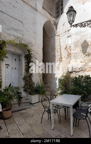 OSTUNI, ITALIEN - 18. OKTOBER 2022: Kleiner Innenhof in der Altstadt mit Tisch und Stühlen Stockfoto