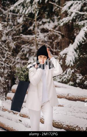 Ein Mädchen in einem weißen Anzug und Balaklava mit einem Paket Weihnachtsbäume im Winterwald an Silvester. Neujahrskonzept Stockfoto