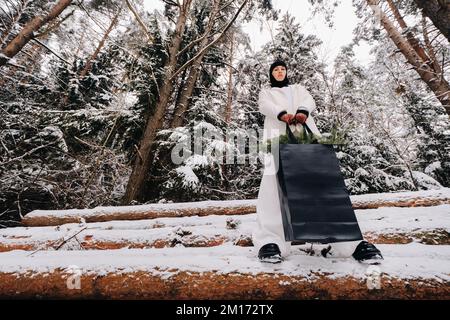 Ein Mädchen in einem weißen Anzug und Balaklava mit einem Paket Weihnachtsbäume im Winterwald an Silvester. Neujahrskonzept Stockfoto