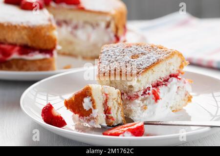 Ein Stück Victoria Kekskuchen mit Schlagsahne, Marmelade und frischen Erdbeeren essen. Stockfoto