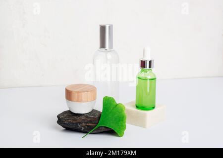 Frisches grünes Ginkgo-Biloba-Blatt, Kosmetikserum und Tonic-Flaschen, Sahnedose auf weißem Tisch. Naturkosmetik-Konzept. Nahaufnahme. Stockfoto