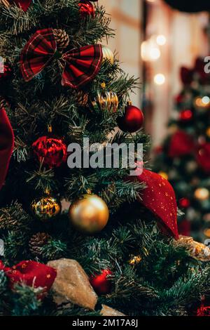 Fantastische Weihnachtsdekorationen auf Tannenbaum mit goldenen und roten Kugeln und Weihnachtslichtern, Nahaufnahme. Stockfoto