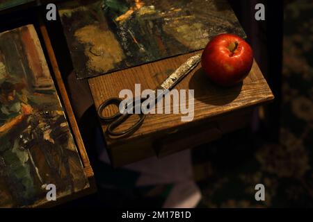 Stilleben mit klassischer schwarzer Schere und Apfel mit Gemälden im Kunststudio Stockfoto