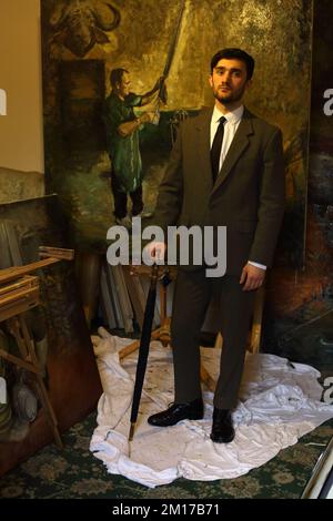 Eleganter Mann in Anzug und Zeh mit einem Regenschirm in einem Künstlerstudio mit Ölgemälde im Hintergrund. Stockfoto