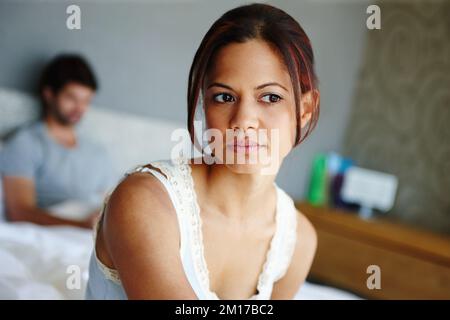Beziehungsprobleme. Aufnahme einer verärgerten Frau, die auf der Seite ihres Bettes mit ihrem Freund im Hintergrund sitzt. Stockfoto