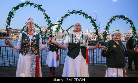 London, Großbritannien. 10.. Dezember 2022. Eine Gruppe mit beleuchteten Girlandringen tritt auf. Der jährliche festliche Morris Dance „Xmas Day of Dance“ ist ein Treffen von etwa 50 Tänzern aus verschiedenen Gruppen, die entlang der South Bank spazieren und in der Nähe der Tate Modern enden, wo sie jeweils den traditionellen mittelalterlichen englischen Tanz für die Öffentlichkeit vorführen. Die Veranstaltung wird von North Wood Morris Men aus Croydon organisiert. Kredit: Imageplotter/Alamy Live News Stockfoto