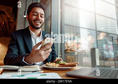 Ein lächelnder indischer Geschäftsmann im Anzug telefoniert während der Mittagspause im Café. Unscharfer Hintergrund Stockfoto
