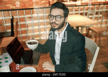 Ein gutaussehender Geschäftsmann im Anzug, der in der Pause Kaffee im Café trinkt und am Fenster sitzt Stockfoto