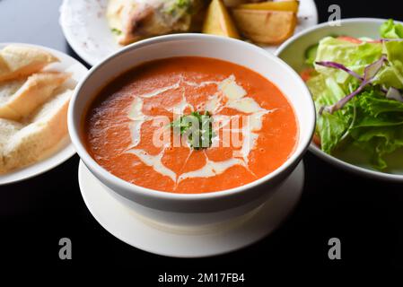 Mittagsset aus Tomatencremesuppe, Salat, Huhn mit Kartoffeln, Limonade auf schwarzem Hintergrund Stockfoto