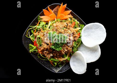 Asiatischer Rindersalat mit Indianerblättern serviert mit Reischips auf schwarzem Hintergrund Stockfoto