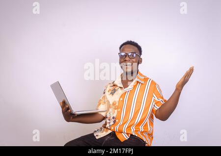 Aufgeregter junger schwarzer afrikanischer Mann hält einen Laptop und hebt seine Hände in Begeisterung, nachdem er etwas im Internet gewonnen hat, isoliert auf weißem Hintergrund. C Stockfoto