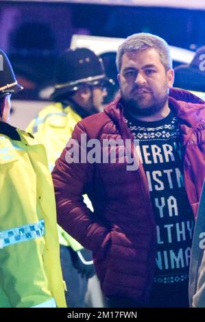 Broad Street, Birmingham, 10. 2022. Dezember - Ein Mann sprach mit Polizisten, nachdem 2 weitere am Samstag, 10. Dezember Nacht, in der Broad Street verhaftet wurden. Einer der Täter war blutverschmiert und beide wurden in abwartende Polizeiwagen gefesselt. Die Nacht begann ruhig aufgrund der Niederlage von 2-1 gegen Frankreich. Einige Partygänger wurden auf dem Nachtclub-Strip gesehen, aber einige posierten gerne für ein Foto. Ein Mädchen sagte, sie „bedauere“ es, keinen Mantel zu tragen, da sie mit ihren Armen in einem roten englischen Hemd gesehen wurde, während sie zwischen Clubs ging, bevor sie mit ihrem Freund für ein Foto posierte. Stockfoto