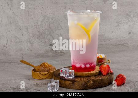 Boba- oder Tapioka-Perlen sind taiwanischer Seifenmilchtee in Plastikbecher mit Erdbeerzitronengeschmack auf Texturhintergrund, Sommererfrischung. Stockfoto