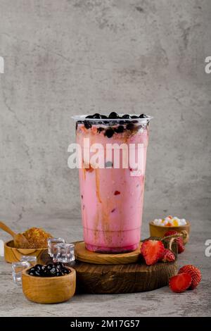 Boba- oder Tapioka-Perlen sind taiwanischer Seifenmilchtee in Plastikbecher mit Erdbeermarmelade auf texturiertem Hintergrund, Sommererfrischung. Stockfoto