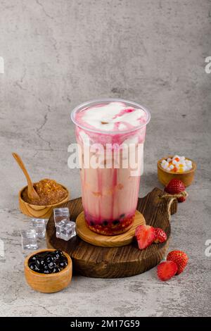 Boba- oder Tapiokapperlen ist taiwan Bubble Milk Tea in Plastikbecher mit Erdbeerkäse Aroma auf texturiertem Hintergrund, Sommererfrischung. Stockfoto