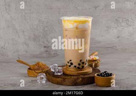 Boba- oder Tapioka-Perlen sind taiwanischer Seifenmilchtee in Plastikbecher mit Kaffee-Karamell-Aroma auf texturiertem Hintergrund, Sommererfrischung. Stockfoto