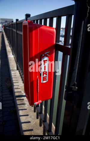 Roter Kamin mit kleinem Hammer in der Nähe und verbunden mit einem Metallzaun am Yachthafen in der Nähe der Docks Stockfoto