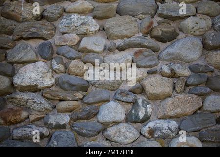 Unterschiedlich große Felsen mit verschiedenen Formen und Farben, die wie die Wand eines Gebäudes angeordnet sind Stockfoto