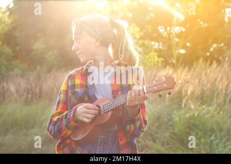 Unschärfe-Mädchen mit Gitarre bei Sonnenuntergang. Ein Mädchen, das in der Natur herumläuft. Ein kleines Mädchen draußen auf der grünen Wiese. Sommerzeit. Ein Volkskünstler Stockfoto