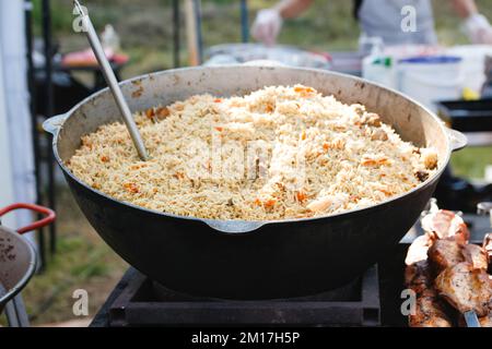 Unschärfe Rühren des Pilafs in einer großen Schüssel beim Kochen im Freien. Nationalgericht. Kochen von traditionellem Pilaf in einem großen Kessel, Street Food im Haus Stockfoto