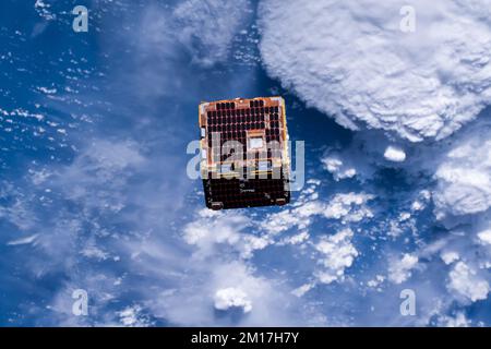 Kleiner Satellit, der den Weltraum über der Erde umkreist, eingesetzt von der internationalen Raumstation. Digital optimiert. Bildelemente von der NASA Stockfoto
