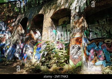 Farbenfrohe bemalte Graffiti auf alten, stillgelegten Backsteinbögen in der Sonne entlang des Parkland Walk in der Nähe von Finsbury, Archway und Highgate, London, England Stockfoto
