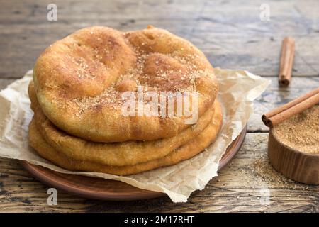 Hausgemachtes gebratenes Navajo-Brot oder süße Elefantenohren mit braunem Zucker und Zimt auf einem Holztisch, selektiver Fokus Stockfoto