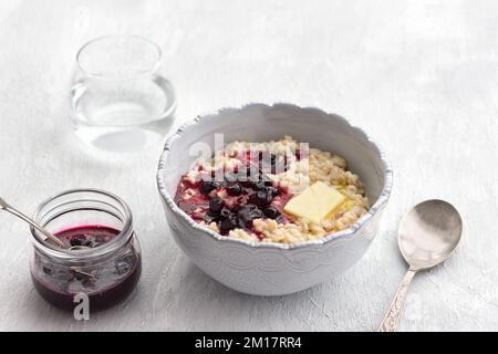 Köstlicher Haferbrei mit Butter und Marmelade in einer grauen Schüssel auf hellgrauem Hintergrund. Gesundes, hausgemachtes Frühstück. Selektiver Fokus, Raum Stockfoto