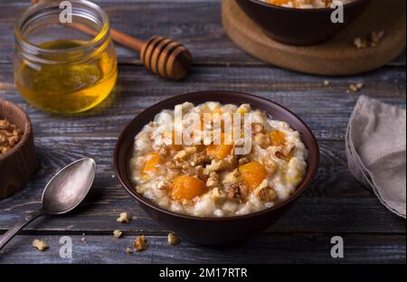 Köstlicher Haferbrei mit gebackenem Kürbis, Honig und Nüssen in einer Keramikschüssel auf einem Holztisch. Gesundes, hausgemachtes Frühstück. Selektiver Fokus Stockfoto