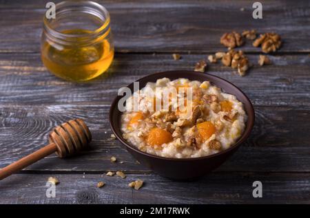 Köstlicher Haferbrei mit gebackenem Kürbis, Honig und Nüssen in einer Keramikschüssel auf einem Holztisch. Gesundes, hausgemachtes Frühstück. Selektiver Fokus Stockfoto